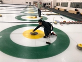 Curler lunged down on the ice, holding a curling rock, getting ready to push off